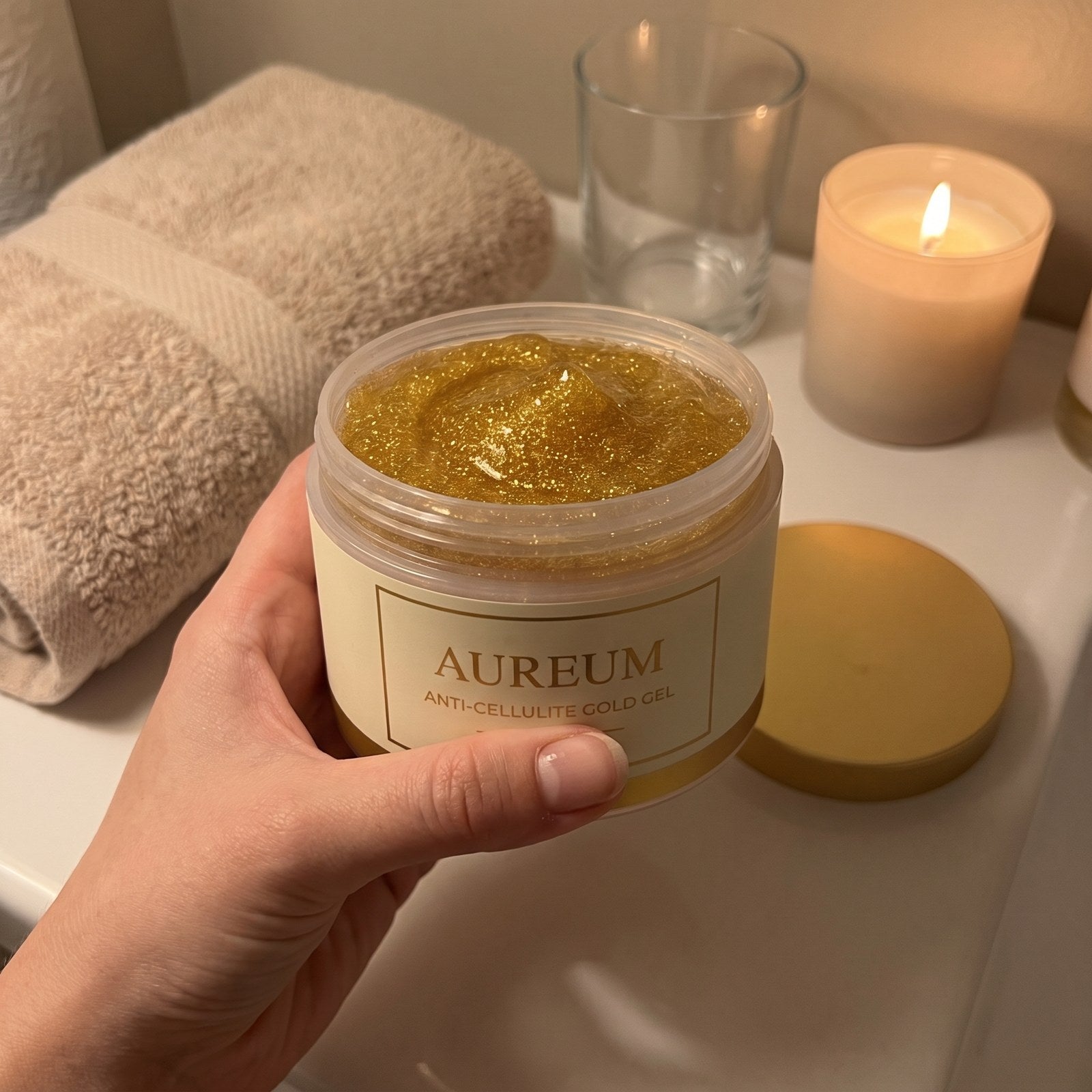 A hand holding the open AUREUM tub on a bathroom counter in evening lamplight