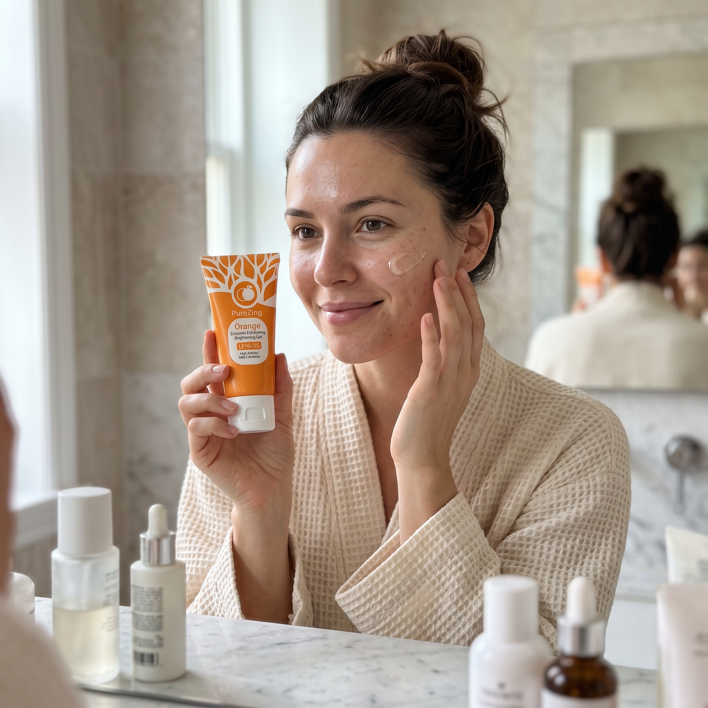 Woman holding PureZing Orange Enzyme Brightening Gel at a bright bathroom vanity