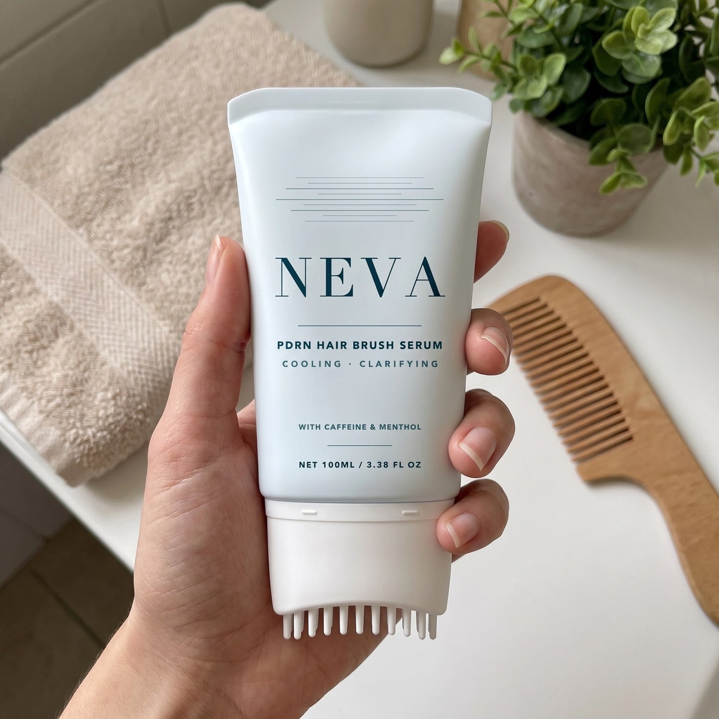 A hand holding the NEVA tube on a bathroom counter beside a wooden comb