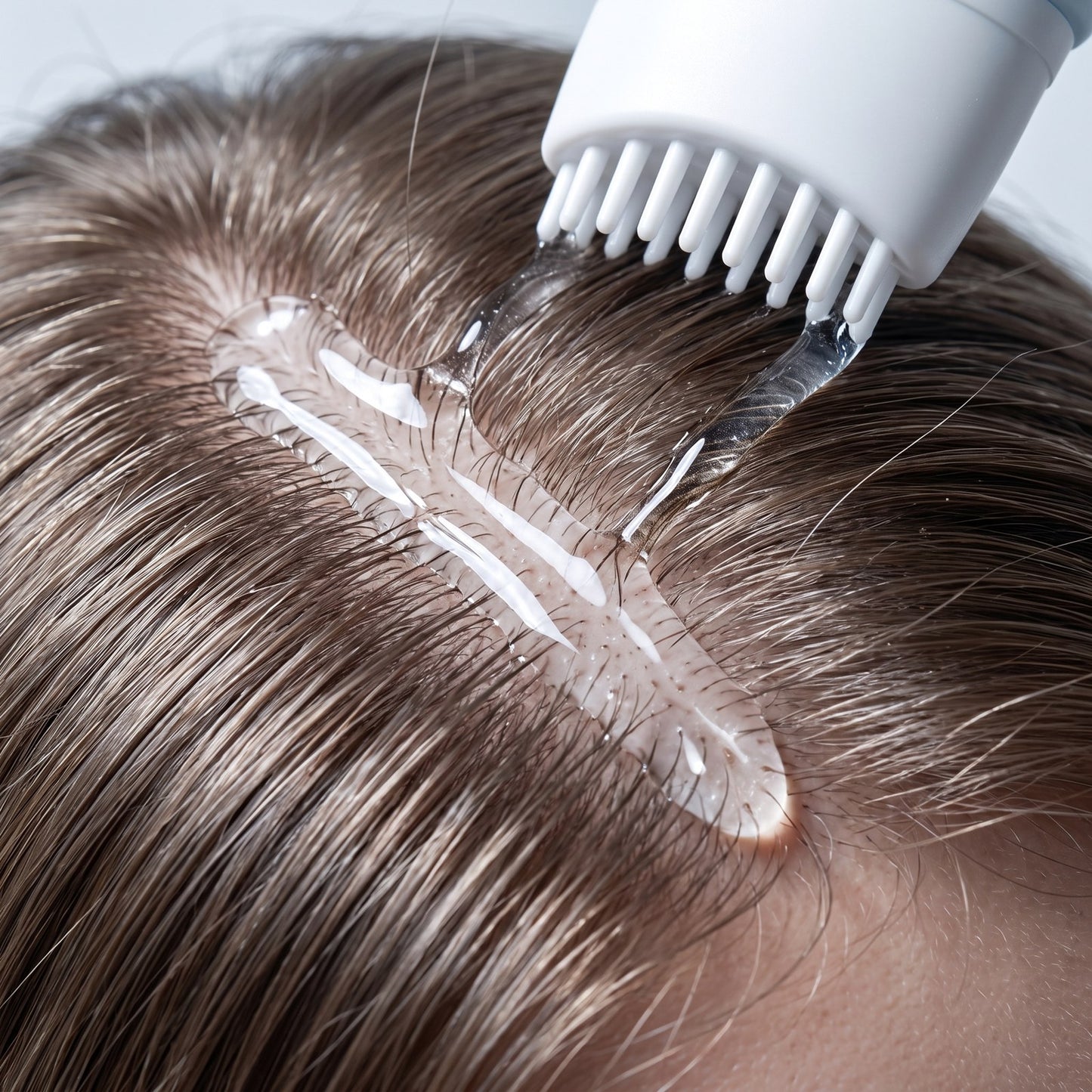 Close view of clear NEVA serum sitting along the scalp parting with the applicator teeth in contact