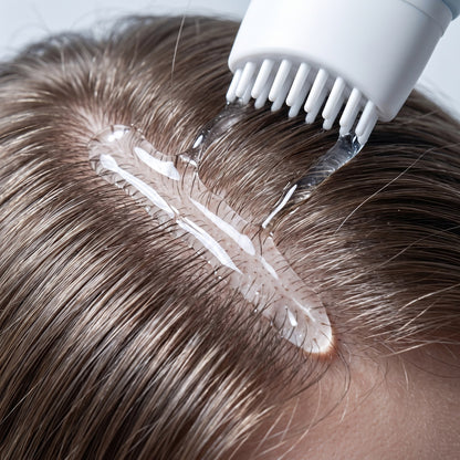 Close view of clear NEVA serum sitting along the scalp parting with the applicator teeth in contact