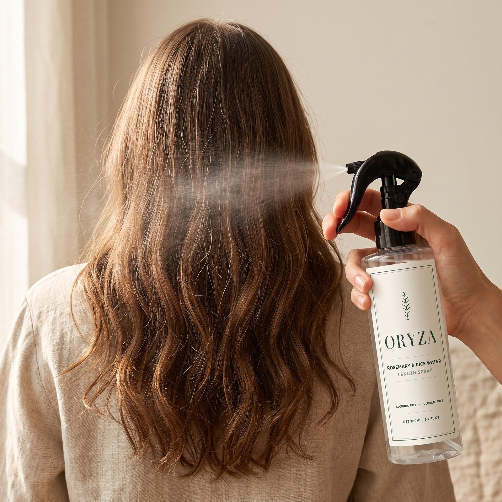 A woman seen from behind misting ORYZA Rosemary and Rice Water Length Spray through the mid-lengths of her long hair