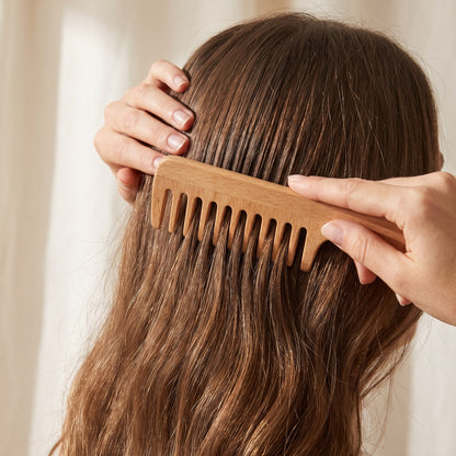 A wide-tooth wooden comb passing cleanly through the mid-lengths of long hair without snagging