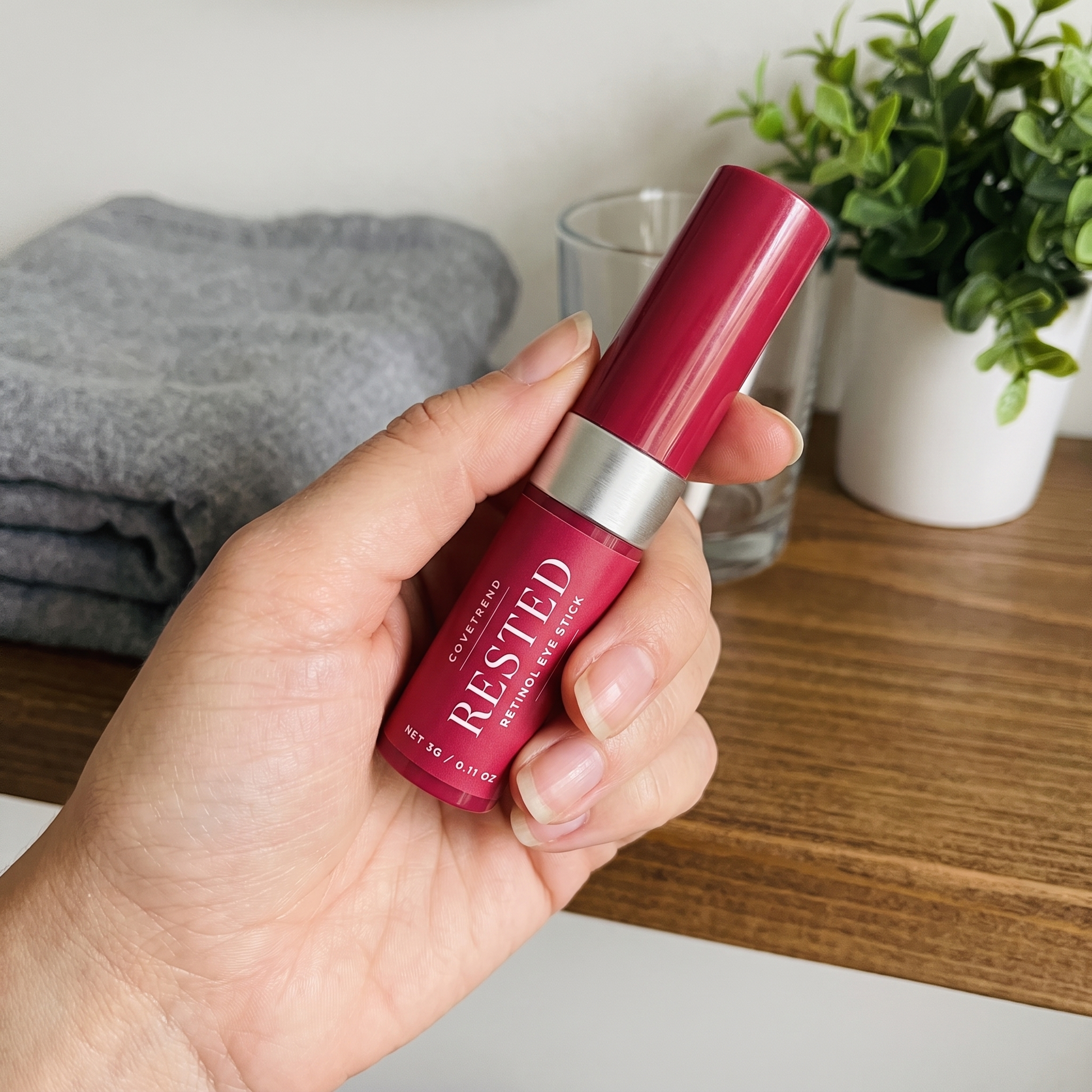 Holding RESTED retinol eye stick on a bathroom shelf